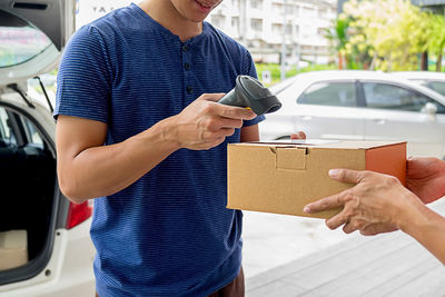 Midsection of delivery man scanning box held by person