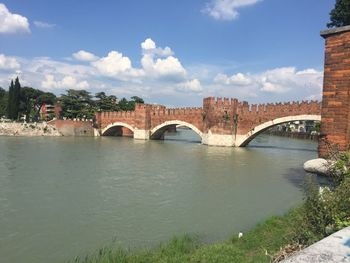 Arch bridge over river amidst buildings against sky