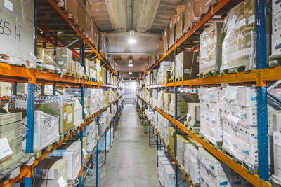 From above of empty narrow passage between big metal shelves with different packages and boxes in warehouse