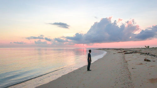 Full length of man standing at beach against sky during sunset