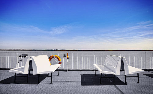 Lounge chairs and chair by sea against blue sky