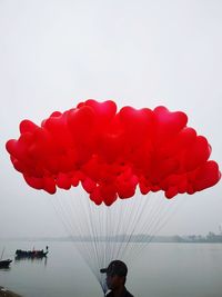 Low angle view of man holding red balloons against sky