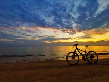 Bicycle on beach against sky during sunset