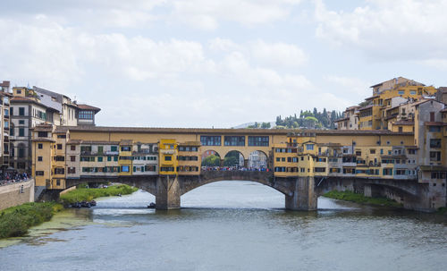 Arch bridge over river by buildings against sky in city