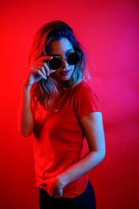 Young woman wearing sunglasses standing against red wall