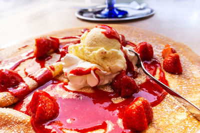 Close-up of pancake garnished with ice cream and strawberries served in plate