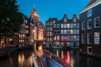 View of river in front of illuminated buildings against blue sky