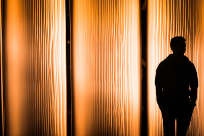 Silhouette man standing against illuminated curtain