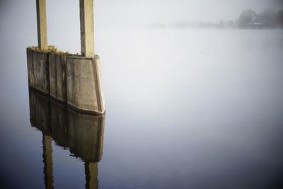 Wooden post in lake against sky