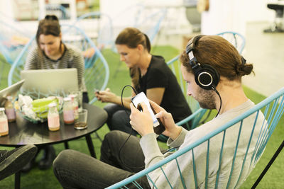 Businessman listening music through smart phone with colleague at office canteen