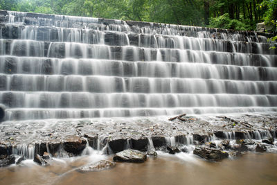 Full frame long exposure tiered waterfall. green foliage background and smooth water in foreground.