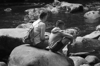 Rear view of people sitting on rock looking at waterfall