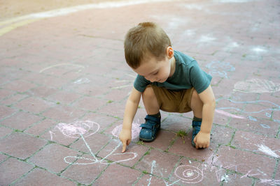 Little toddler boy two or three years old points his finger at children's drawings drawn in chalk. 