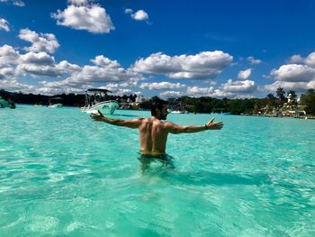 Rear view of shirtless man with arms outstretched standing in sea against sky