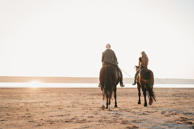 People riding horse on beach against sky