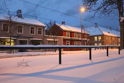 Houses on snow covered field by buildings against sky