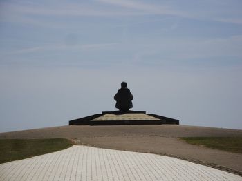 Statue of man sitting against sky