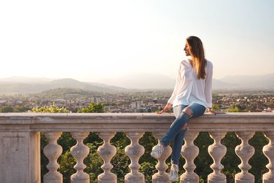 Woman sitting on balustrade against landscape

