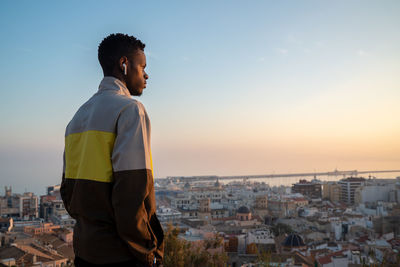 Man looking at city buildings against sky during sunset