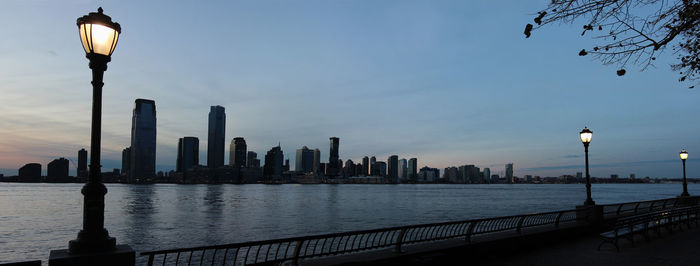 Illuminated street by river and buildings against sky