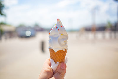 Female hand holds an ice cream cone on a street. ice cream melted and ran down fingers and hand.