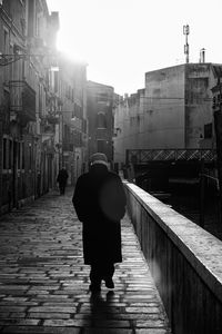 Rear view of woman walking on footpath amidst buildings in city