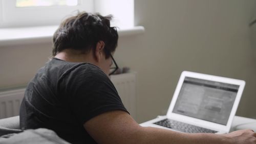 Rear view of man using mobile phone at home