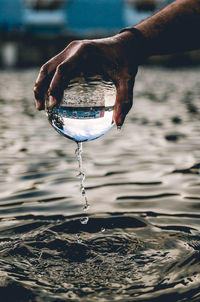 Cropped hand of man holding wet crystal ball over lake