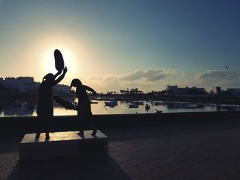 Silhouette statues by sea against sky during sunset