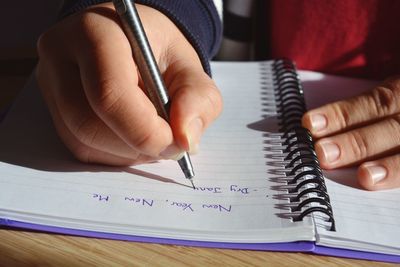 Midsection of person writing in book on table