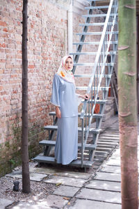 Portrait of young woman standing on steps against brick wall