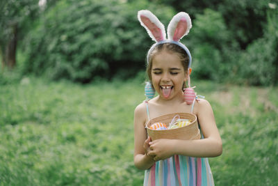 Girl with eggs basket and bunny ears on easter egg hunt in garden.