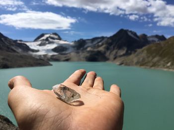 Close-up of hand against lake against sky