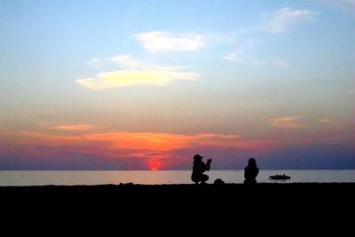 Silhouette people standing on land against sky during sunset
