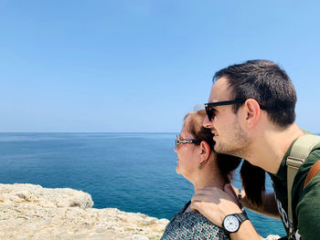 Mother and son wearing sunglasses against blue sea against sky, enjoying a day out in havana.