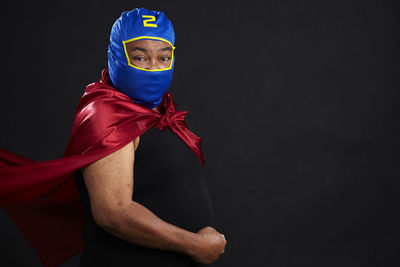 Portrait of man in costume flexing muscles against black background