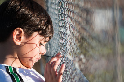 Close-up portrait of boy looking through chainlink fence