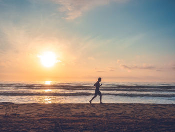 Silhouette of jogging man on beach in the morning at sunrise.