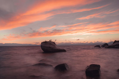 View of rocks in sea against sunset sky