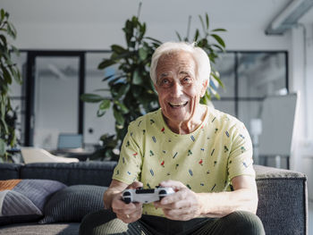 Happy businessman playing video game while sitting on sofa at office