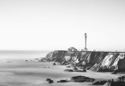 Lighthouse by sea against clear sky