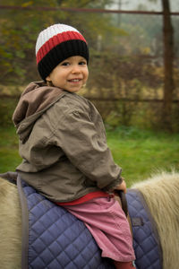 Portrait of cute boy sitting on pony at pen