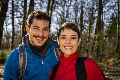 Beautiful young couple is hiking in the woods. the smiling couple looks into the camera.