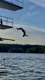 Young man performing a backflip of a jumping platform into a lake. 