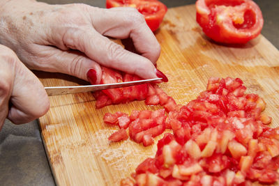 Cropped image of hand holding red chili peppers on cutting board