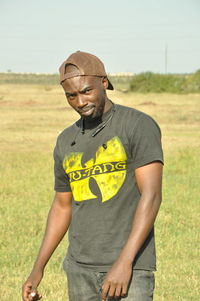 Portrait of young man standing on grass against sky