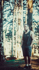 Full length of man standing by tree trunk in forest