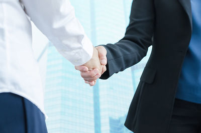 Midsection of business people shaking hands against building