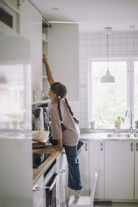 Side view of girl reaching at cabinet in kitchen at home