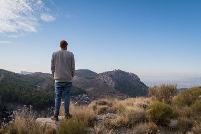 Rear view of man standing on rock against blue sky